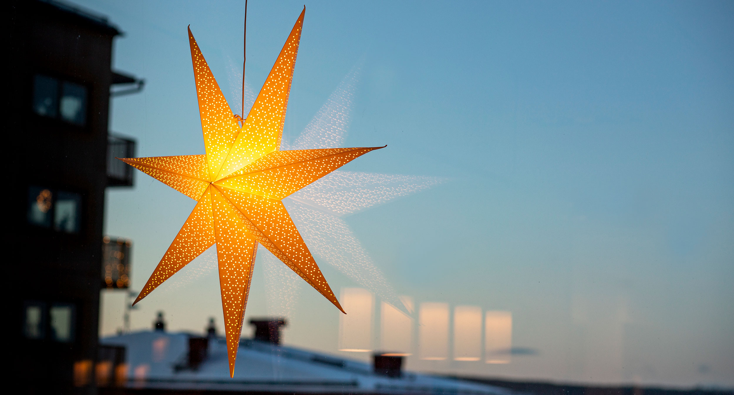 Julstjärna hängande i fönster. Bakom den ser du snötäckta hustak.